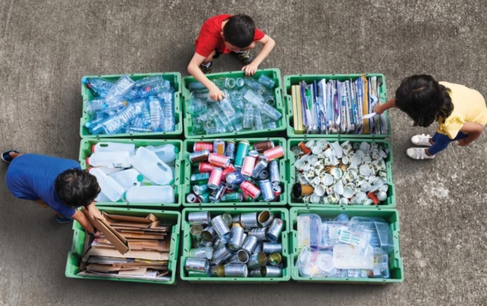 A stock image of three individuals sorting waste materials according to respective categories prior to recycling them.