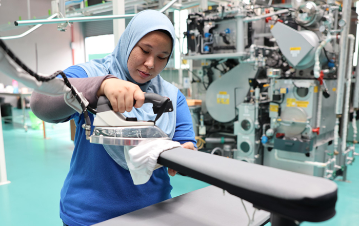 A medium landscape shot of a Sunway Pristine Laundry staff carefully ironing a garment using a Sankosha industrial steam press iron machine.