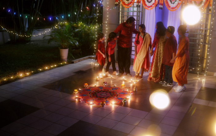 A far shot of an Indian family standing amidst the kolam, in a nicely lit house