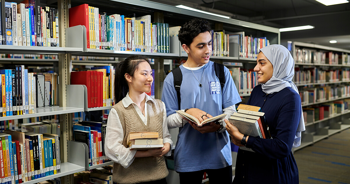 Students chatting in Sunway College Library holding books diversity students. 