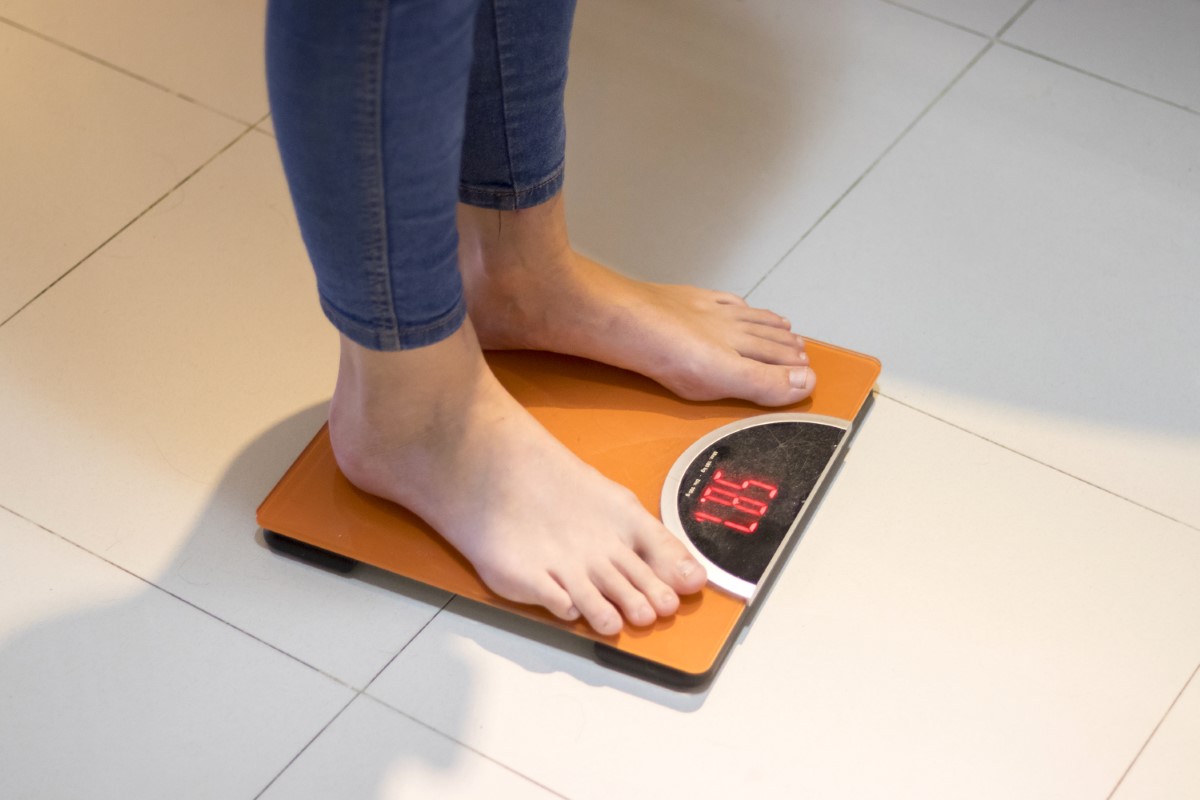 Low section of man standing on a weighing scale on tiled floor