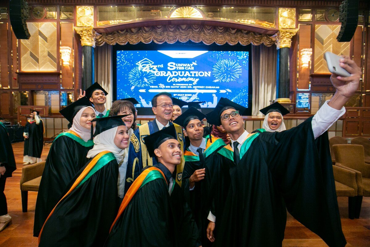 Tan Sri Sir Dr Jeffrey Cheah taking a photo with young graduates at a graduation ceremony