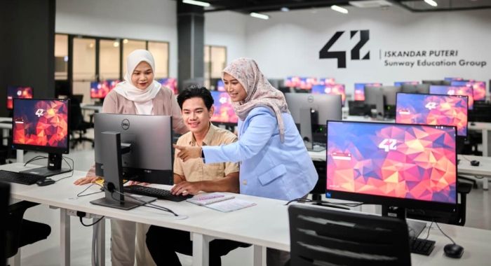 A mid-shot of three students at 42 Iskandar Puteri, pointing at the screen amidst computers around them