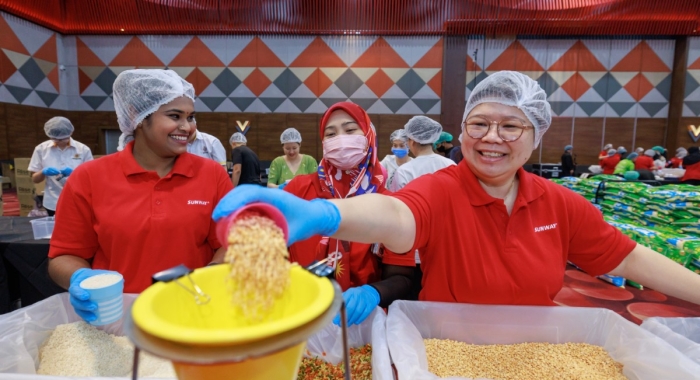 A mid shot of Sunway staff at Sunway Meal Pack-a-Thon 2024, smiling and pouring rice into the chute.