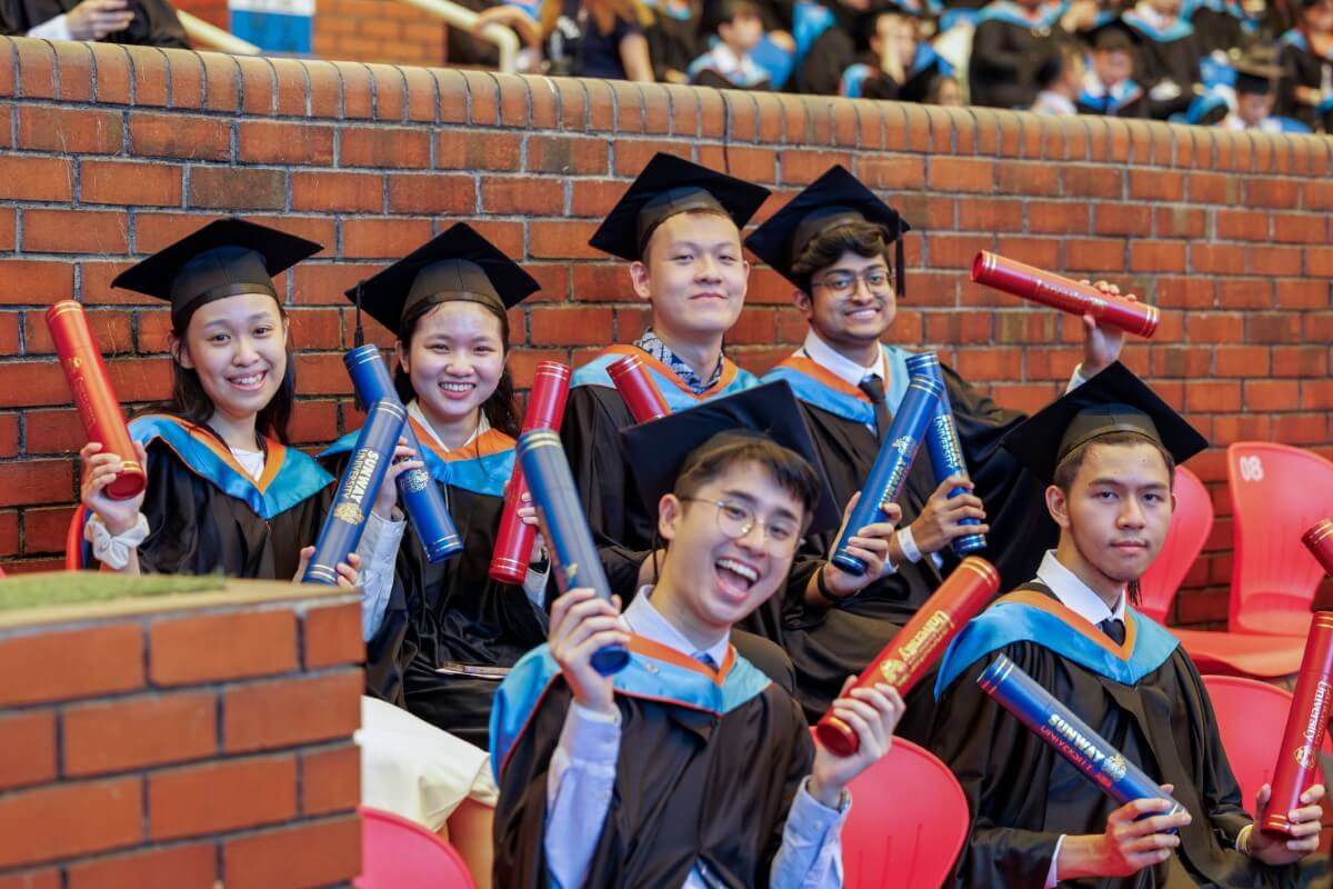 A mid-shot of Sunway University students graduating, holding the scrolls of Sunway University & Lancaster University